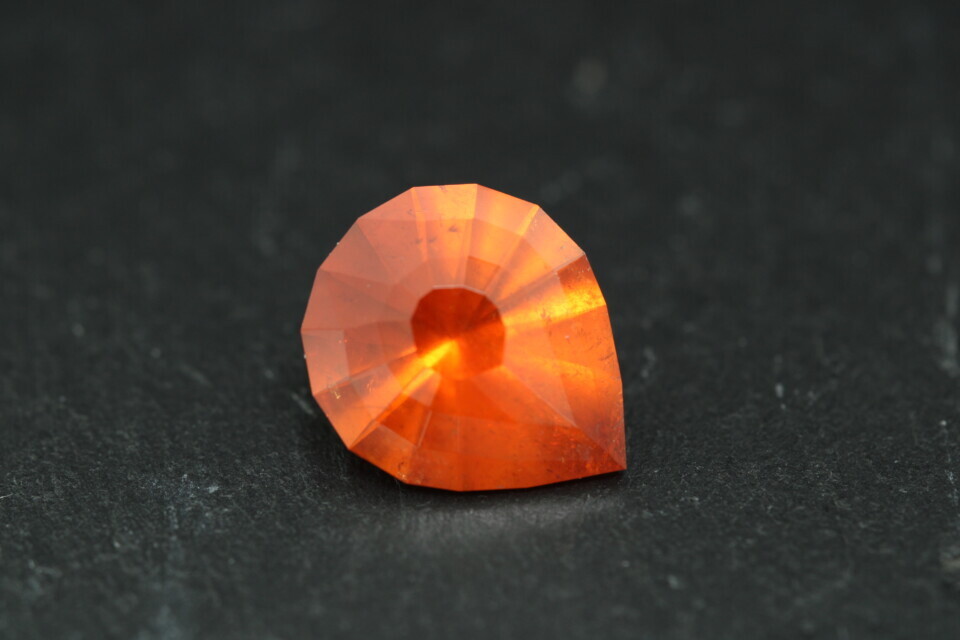 Macro-opname van een 5.3 karaat oranje spessartien granaat in Aqua Drop slijpvorm op zwarte leisteen
