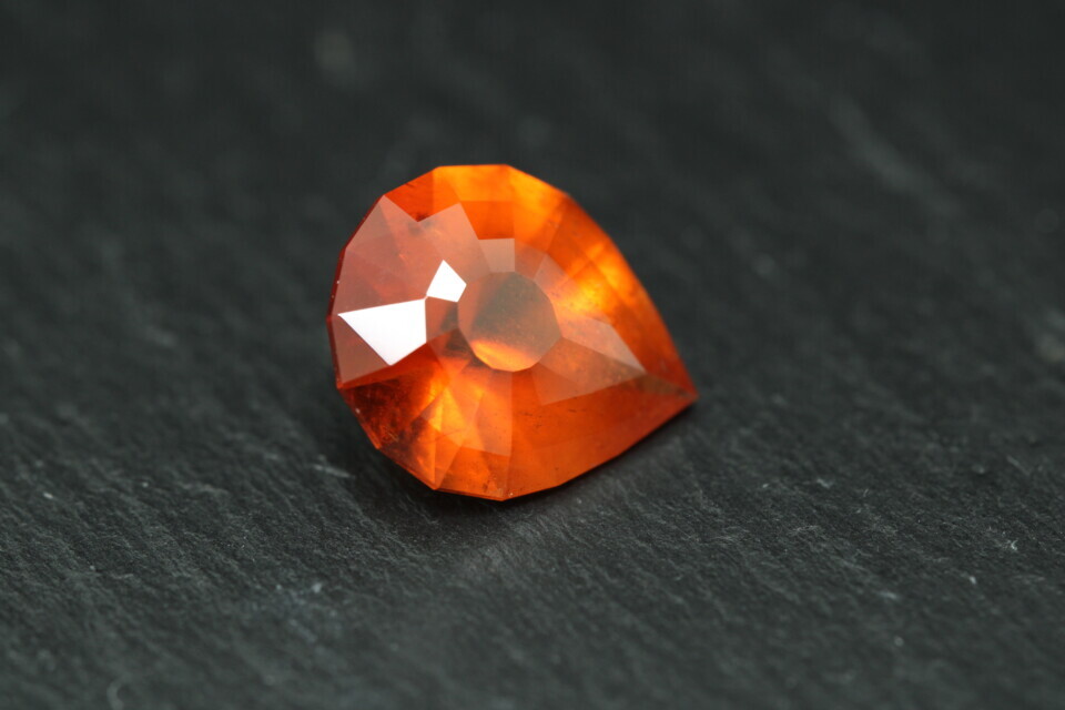 Macro-opname van een 5.3 karaat oranje spessartien granaat in Aqua Drop slijpvorm op zwarte leisteen