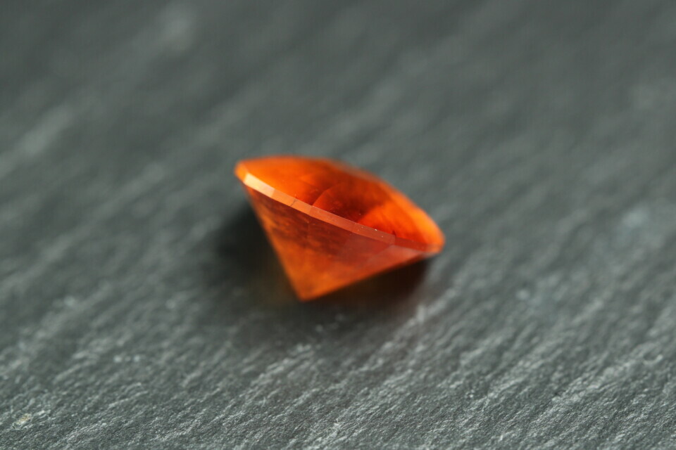 Macro-opname van een 5.3 karaat oranje spessartien granaat in Aqua Drop slijpvorm op zwarte leisteen