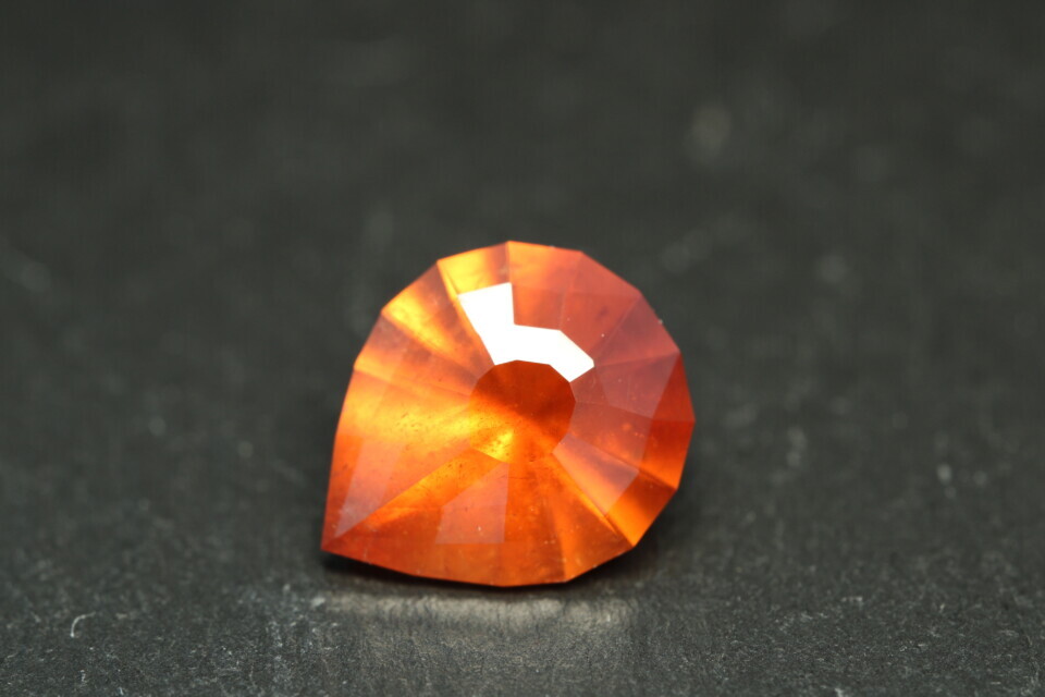 Macro-opname van een 5.3 karaat oranje spessartien granaat in Aqua Drop slijpvorm op zwarte leisteen
