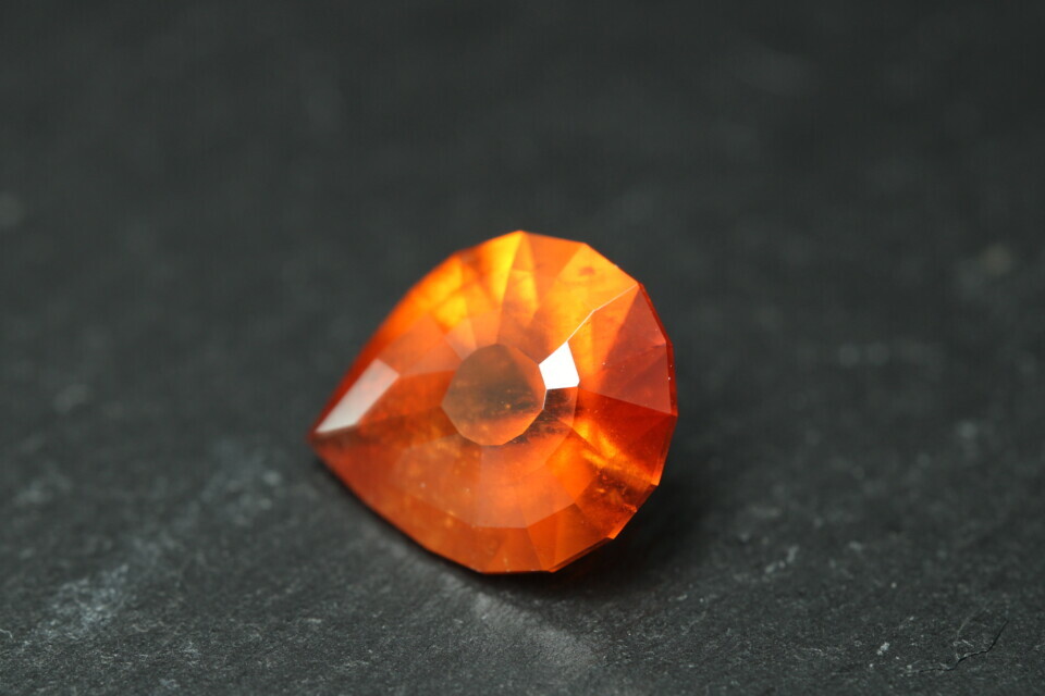 Macro-opname van een 5.3 karaat oranje spessartien granaat in Aqua Drop slijpvorm op zwarte leisteen